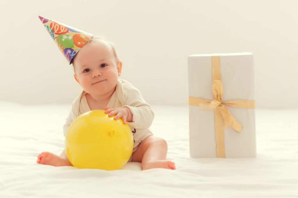 dziecko w czapeczce urodzinowej z balonem i prezentem podczas swoich pierwszych urodzin